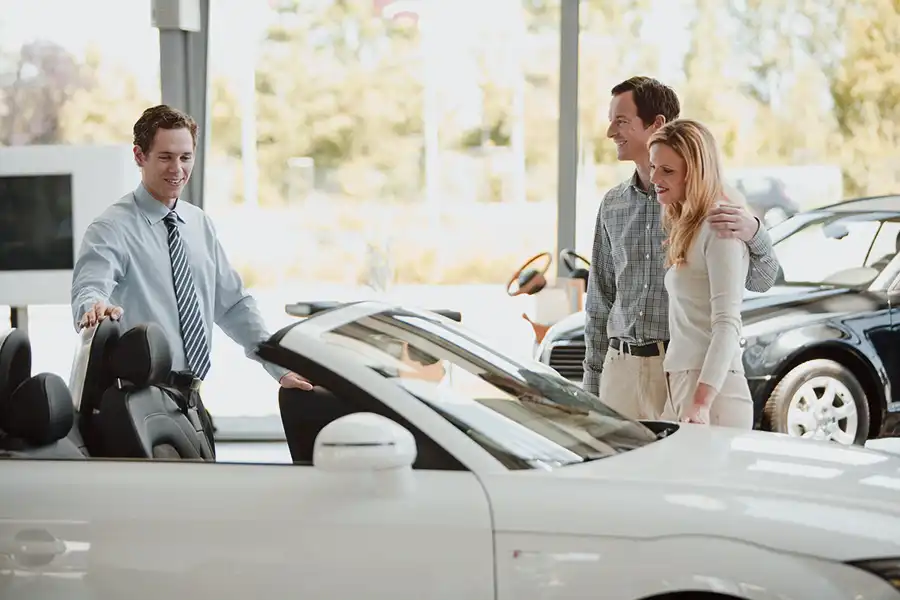Car salesman showing a couple a convertible, symbolizing automobile insurance coverage.